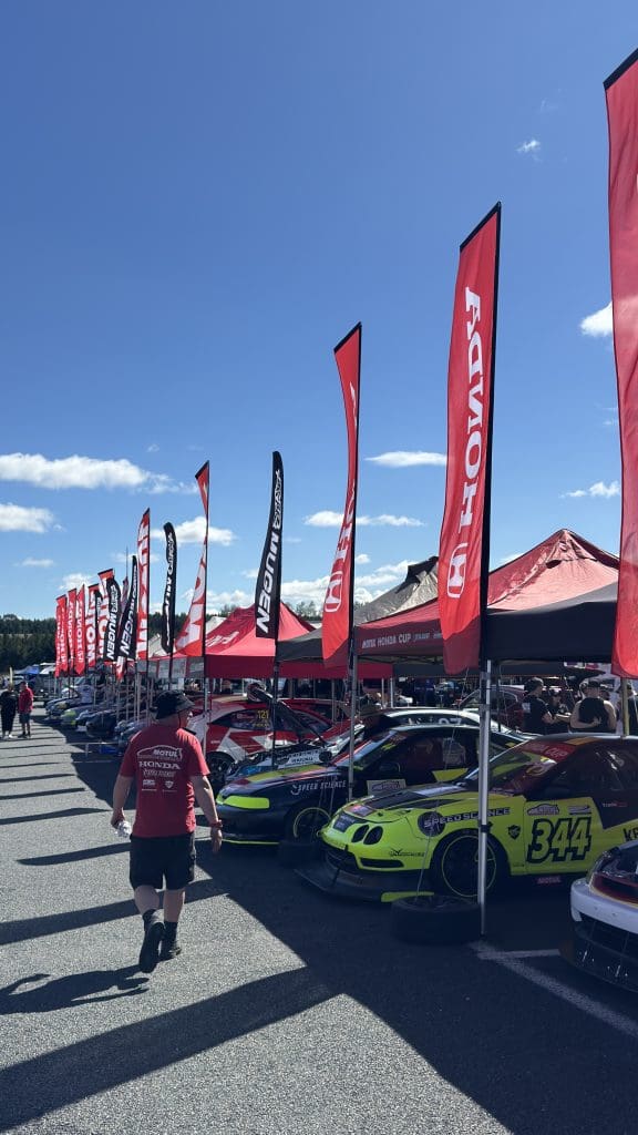 a lineup of Honda Cup cars parked in a asphalt pit area with tents and Honda banners setup overhead