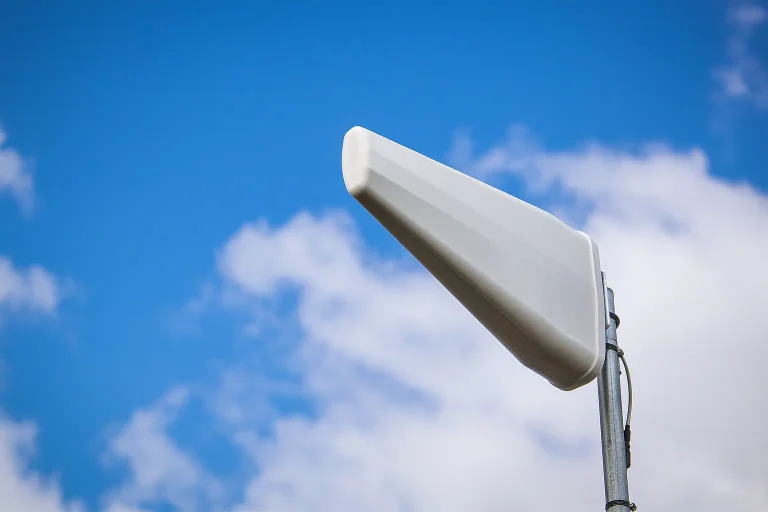 Single-polarity Rural Broadband Initiative antenna mounted on a pole with a blue sky and light clouds in the backround.