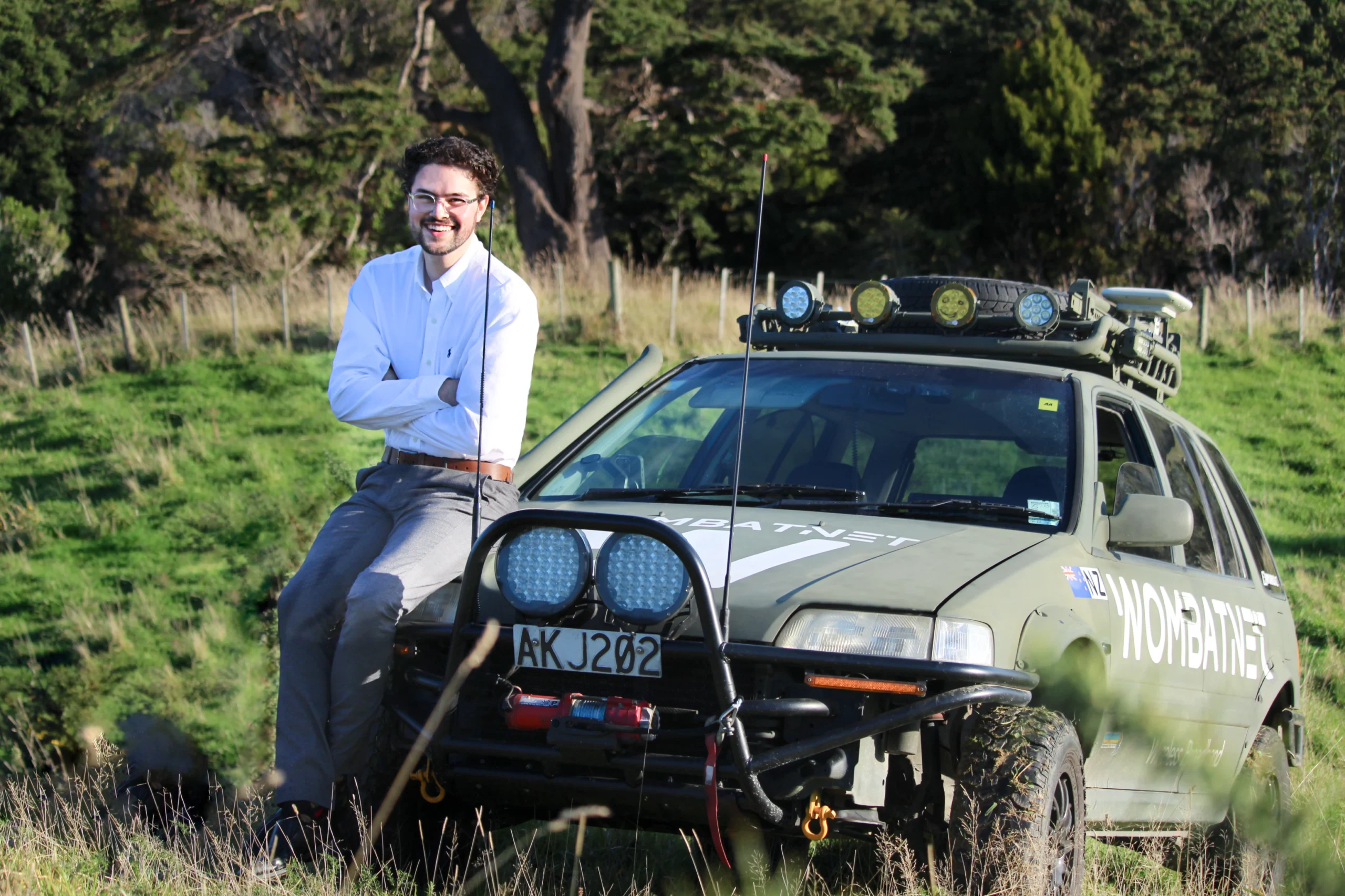 WombatNET Founder Alex Stewart smiling with his arms crossed, leaning against the green WombatNET company car, with a rural green pasture in the background.
